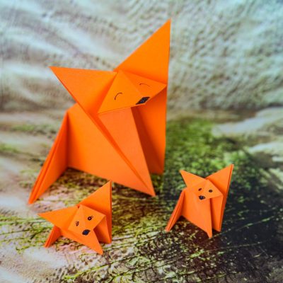 A closeup shot of three orange paper origamis with faces drawn on them on a patterned surface
